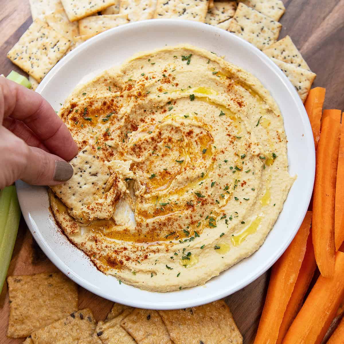 Cracker being dipped into a bowl of creamy homemade hummus.