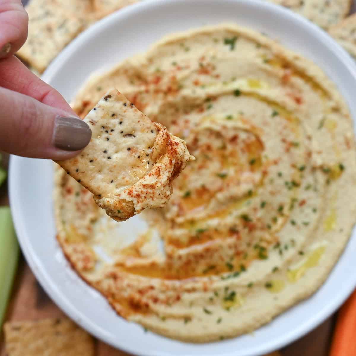 Cracker topped with a scoop of creamy hummus ready to eat.