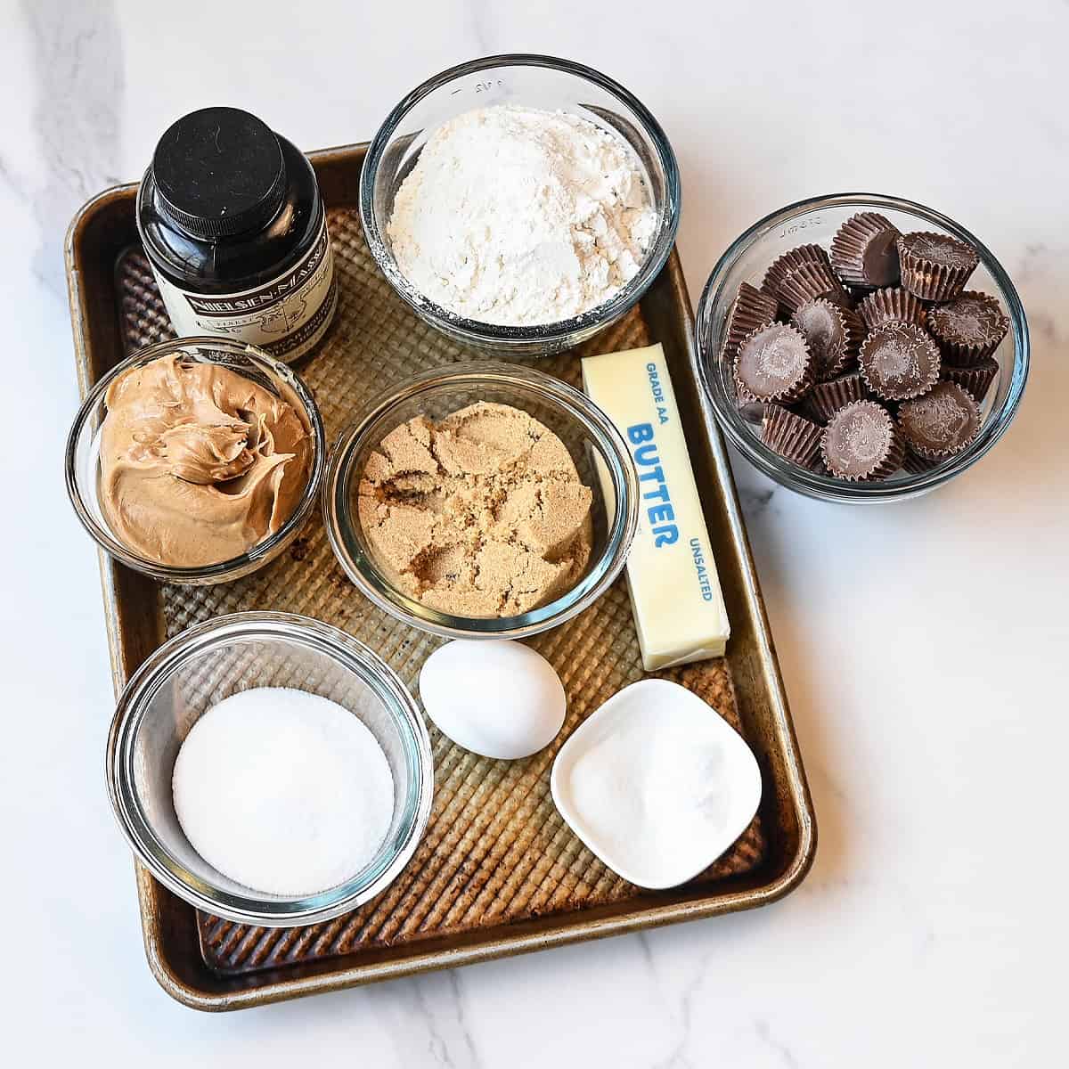 Ingredients for peanut butter cup cookies including peanut butter cookie dough ingredients and mini peanut butter cups arranged on a counter.