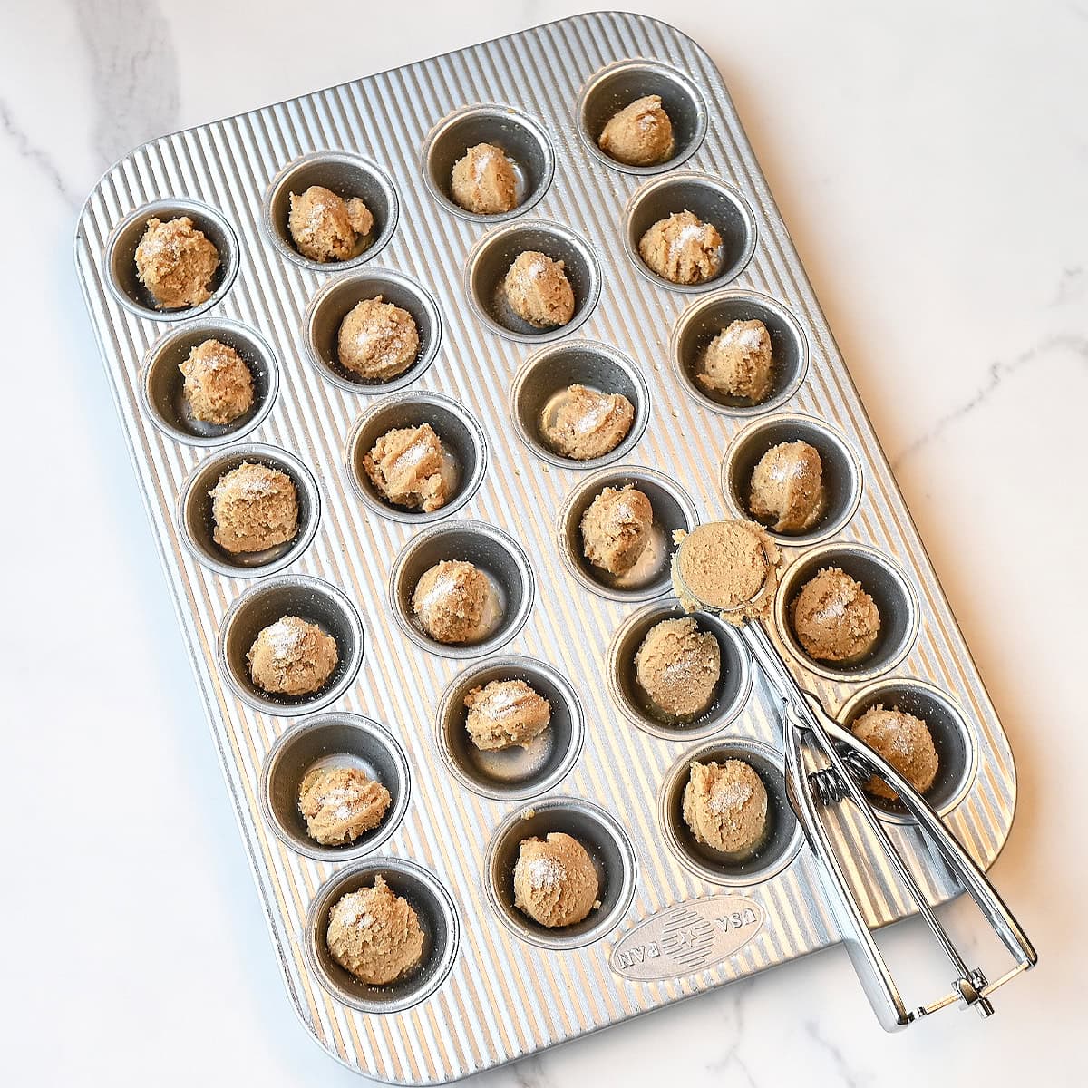 mini muffin pan showing scooped peanut butter cup cookies not being rolled