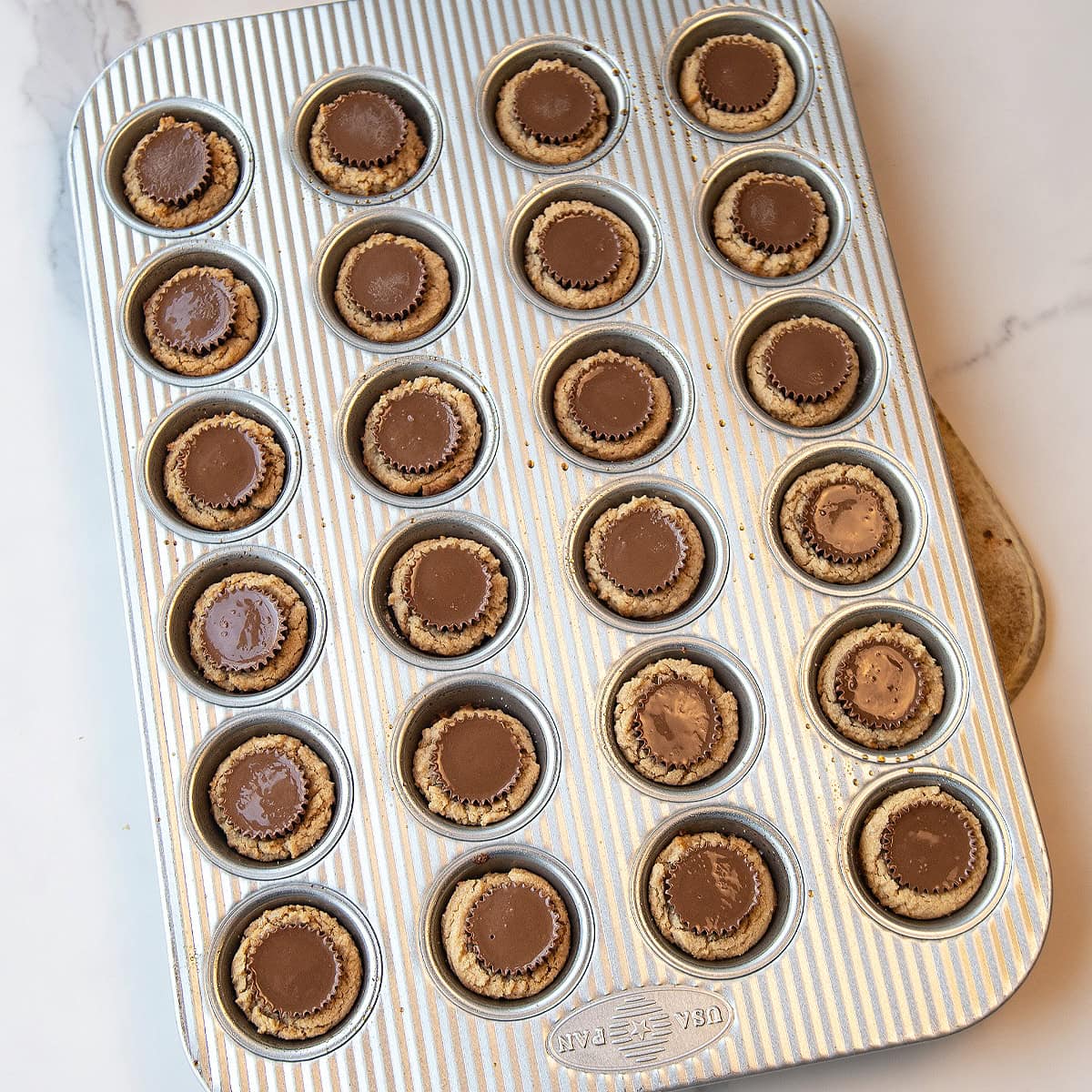 mini muffin pan showing baked peanut butter cup cookies with candies inserted