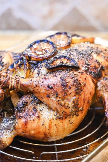 Whole roasted chicken with golden crispy skin resting in a roasting pan with herbs.