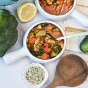 A white bowl filled with healthy white bean vegetable soup full fresh veggies.