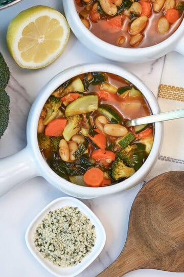 A white bowl filled with healthy white bean vegetable soup full fresh veggies.