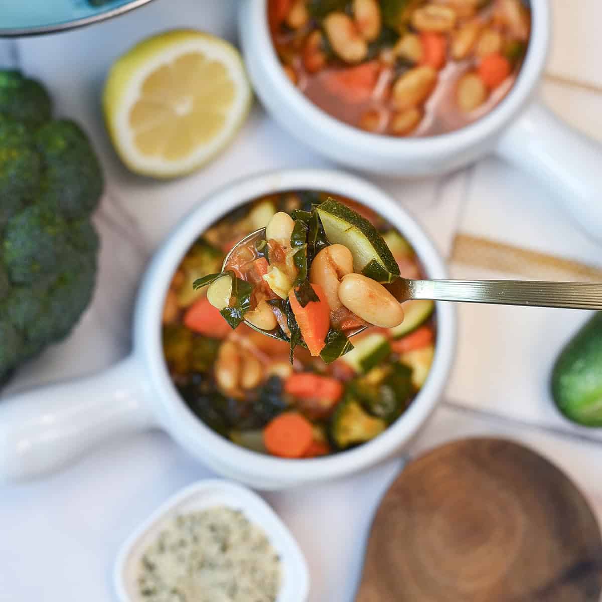 Close-up spoonful of white bean vegetable soup showing vegetables, broth, and cannellini beans.