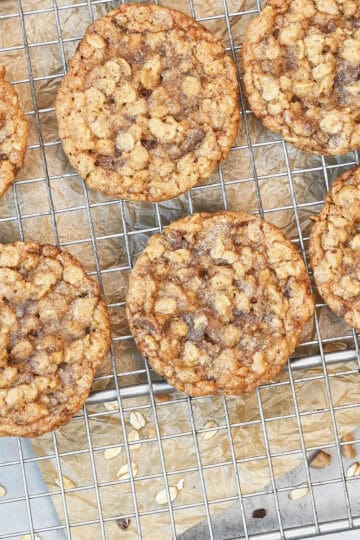 Overhead view of chewy oatmeal toffee cookies cooling on a wire rack with melted toffee pieces and golden brown edges.