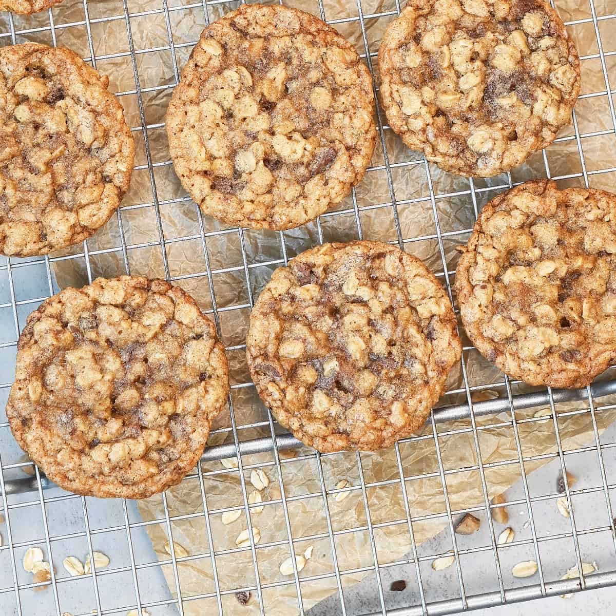 Overhead view of chewy oatmeal toffee cookies cooling on a wire rack with melted toffee pieces and golden brown edges.
