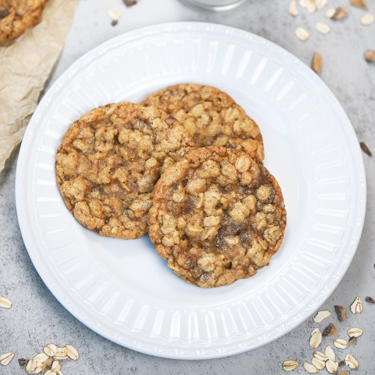 Stack of three chewy oatmeal toffee cookies on a white plate with visible oats and sweet toffee pieces.