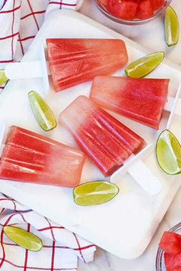 Overhead view of homemade watermelon lime popsicles arranged on a white serving platter, ready to enjoy on a hot summer day.