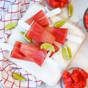 Stack of watermelon lime popsicles garnished with fresh lime slices on a white platter.
